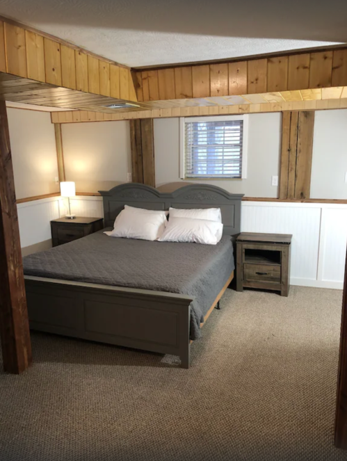 Cozy bedroom featuring a gray bed, two nightstands, and wooden accents on the walls and ceiling.