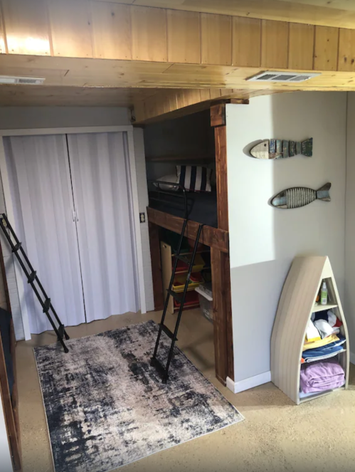 Cozy room with a lofted bed, two ladders, a rug, and storage shelves, featuring wooden accents and fish decor.