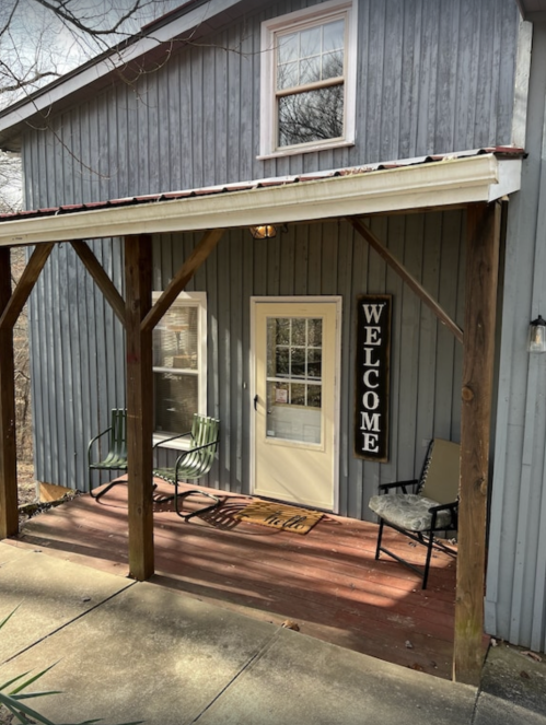 A cozy gray house with a welcoming porch, featuring a "WELCOME" sign and two chairs.