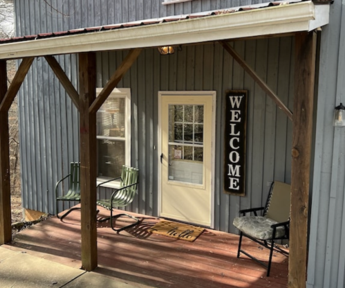 A welcoming porch with two chairs, a "WELCOME" sign, and a door on a gray wooden building.