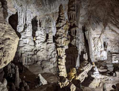 Stalactites and stalagmites in a dimly lit cave, showcasing intricate rock formations and textures.
