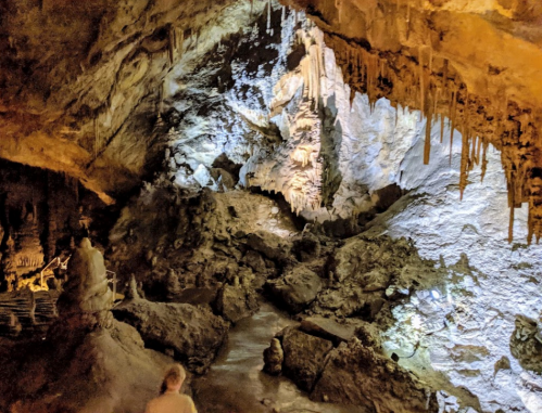 A dimly lit cave interior with stalactites, rock formations, and a small stream, showcasing natural geological features.