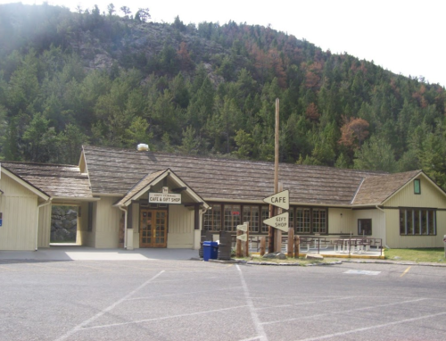 A rustic cafe and gift shop building surrounded by trees and mountains, with a parking area in front.