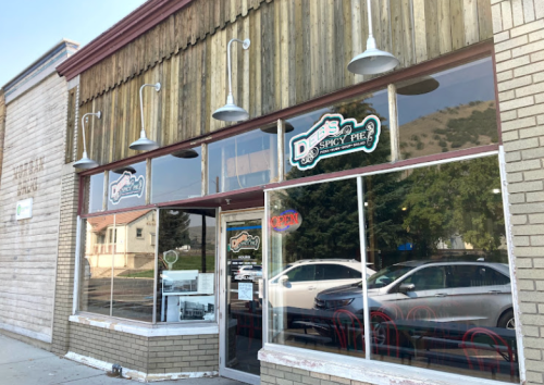 Exterior of a restaurant named "D's Spicy Pie," featuring large windows and a wooden facade. Open sign visible.