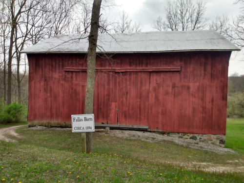 Red barn with a metal roof, surrounded by trees, featuring a sign that reads "Fallas Barn CIRCA 1894."