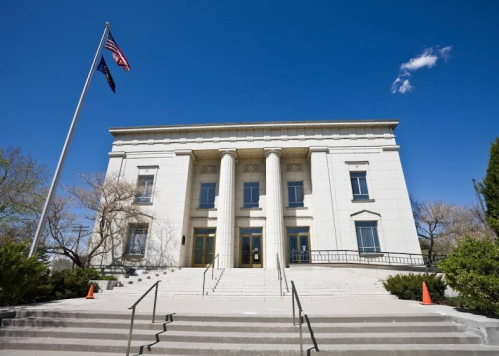 A grand building with columns, steps, and flags, set against a clear blue sky.