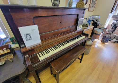 A vintage piano with a bench, displayed in a room with various antique items and a biography on the side.