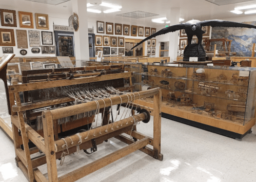 A museum display featuring wooden artifacts, including a loom and glass cases with various historical items.