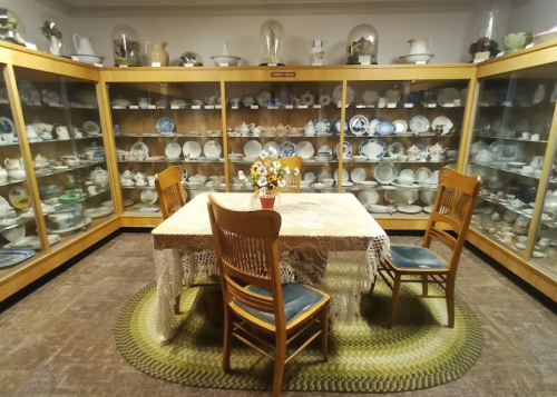 A cozy display room with glass cabinets filled with dishes, a table with a lace tablecloth, and wooden chairs.
