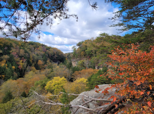 A scenic view of a valley surrounded by colorful autumn foliage under a partly cloudy sky.