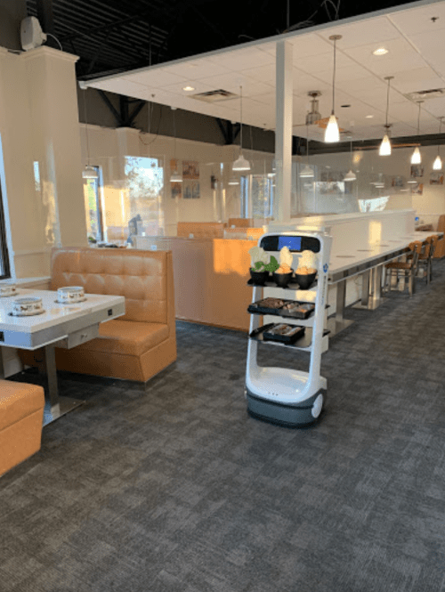 A restaurant interior featuring booths and a service robot on a carpeted floor, with bright lighting and modern decor.