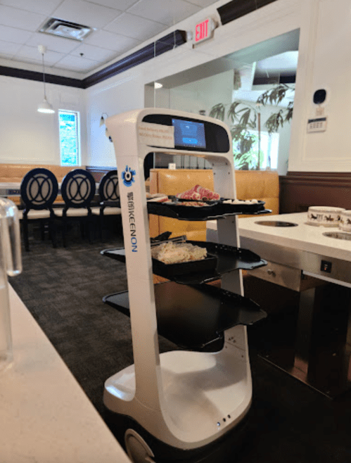 A robotic food delivery cart with multiple shelves, positioned in a restaurant setting.