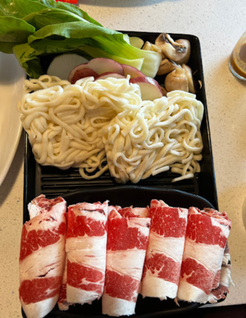 A black tray with thinly sliced beef, noodles, mushrooms, and leafy greens arranged neatly.