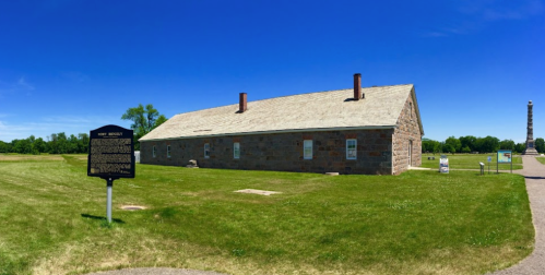 Historic stone building at Fort Brady, surrounded by green grass and a clear blue sky, with a historical marker nearby.