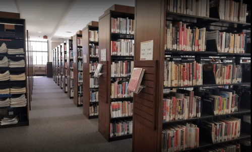 A view of a library aisle lined with tall bookshelves filled with books and periodicals.