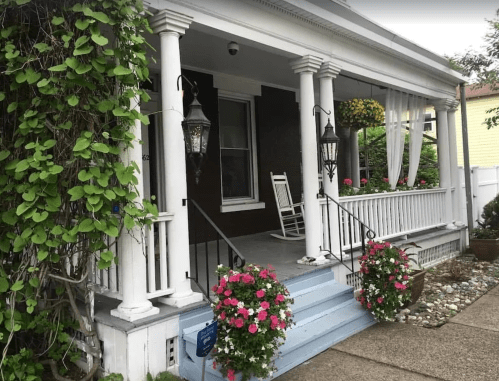A charming porch with white columns, hanging flower baskets, and a rocking chair, surrounded by greenery.