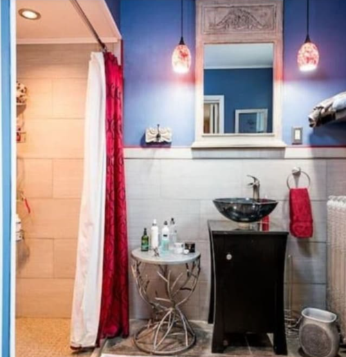 A modern bathroom featuring a black sink, decorative mirror, red accents, and a shower area.