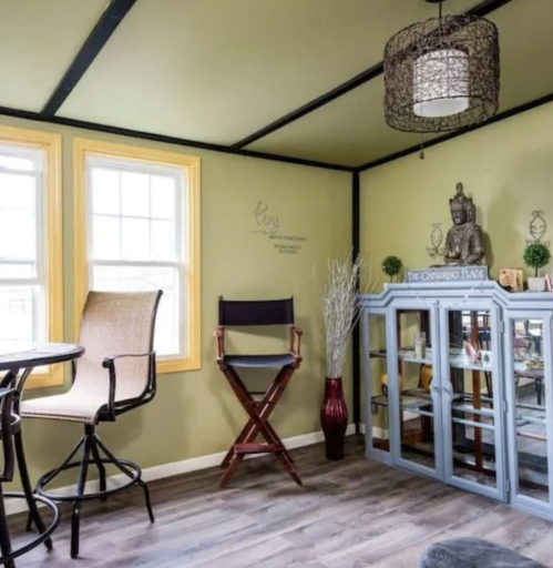 Cozy interior with green walls, a round table, chairs, a display cabinet, and decorative elements like a statue and plants.