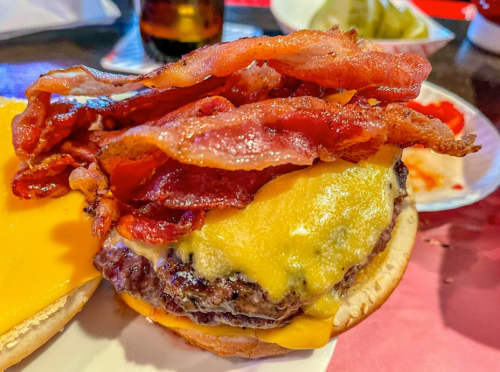 A close-up of a cheeseburger topped with crispy bacon, melted cheese, and served on a bun.