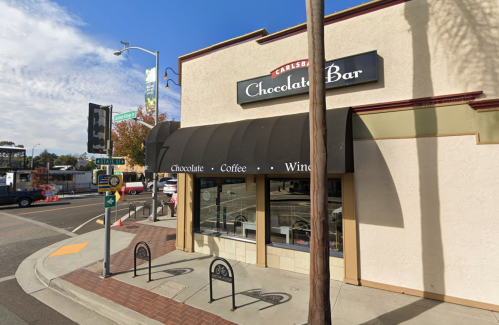 Exterior of a chocolate bar shop with a sign reading "Chocolate Bar" and nearby street signs and bike racks.