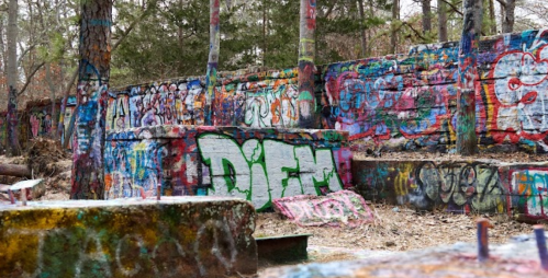 Colorful graffiti covers stone walls in a wooded area, with vibrant designs and messages amidst a natural setting.