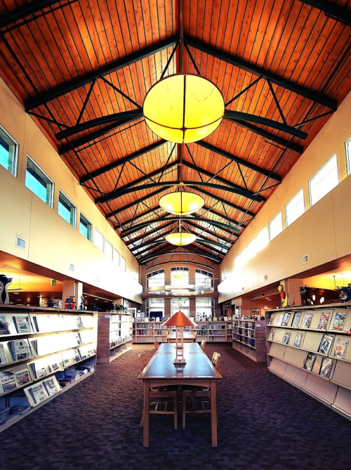 A spacious library interior with high wooden ceilings, bright lights, and bookshelves lining the walls.