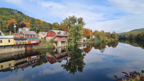 A serene river scene with colorful autumn trees and charming houses reflecting on the water's surface.