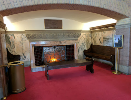 A cozy room featuring a marble fireplace, wooden benches, and a red carpet, with a trash can in the corner.