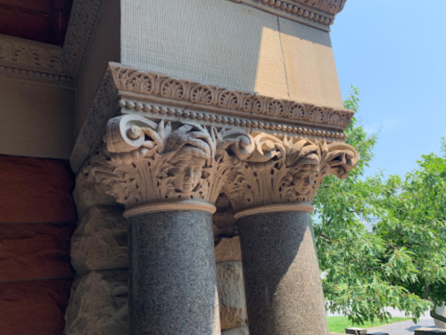 Close-up of ornate stone columns featuring intricate carvings and decorative capitals against a clear blue sky.