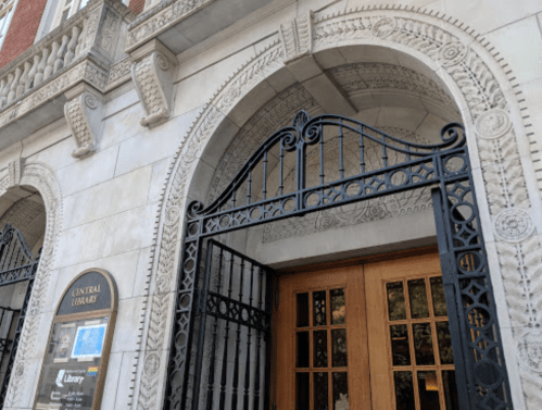 Entrance of a historic library featuring ornate stonework and an intricate wrought iron gate.