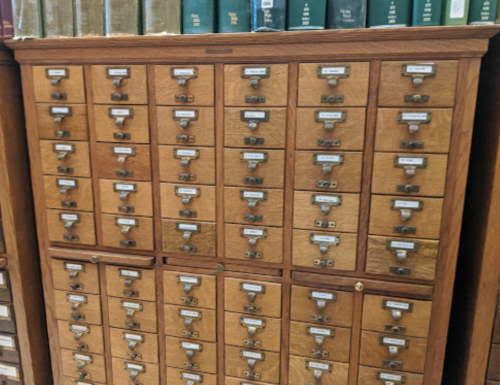 A wooden card catalog with multiple small drawers, each labeled, and books visible on top.