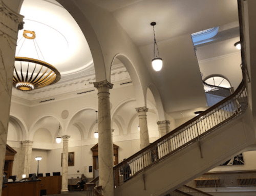 Interior of a grand building featuring arched ceilings, marble columns, and a staircase with elegant lighting.