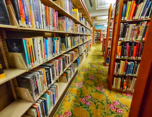 A library aisle lined with bookshelves, featuring colorful carpet with floral patterns.