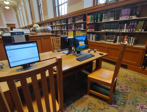 A quiet library space with two computers and wooden chairs, surrounded by shelves of books and globes.