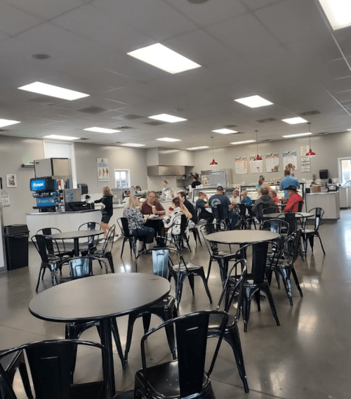 A spacious cafeteria with tables and chairs, featuring a group of people dining and chatting in the background.