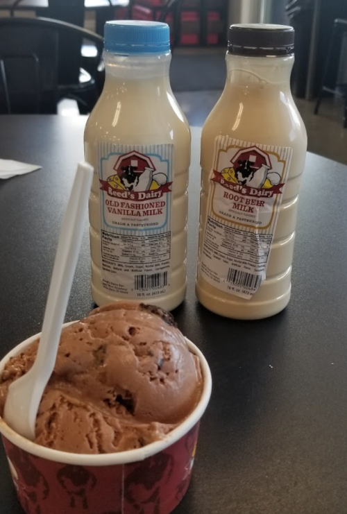 Two bottles of flavored milk (vanilla and root beer) next to a cup of chocolate ice cream with a spoon.