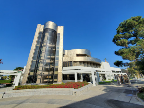 Modern building with a unique design, featuring large glass windows and a golden facade, surrounded by greenery.