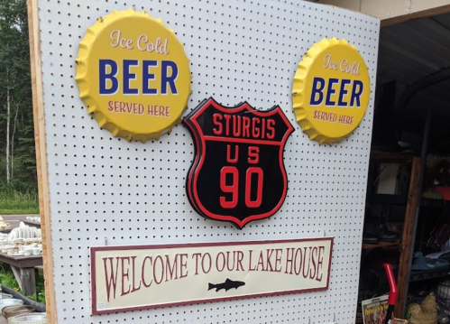 Two beer signs and a Route 90 shield, with a welcome sign for a lake house on a pegboard background.