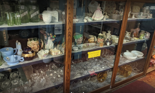 A display cabinet filled with various vintage glassware, ceramics, and decorative items.
