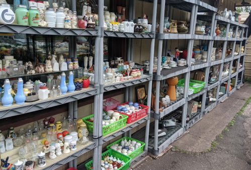 A display of various vintage ceramics and collectibles arranged on shelves outside a shop.