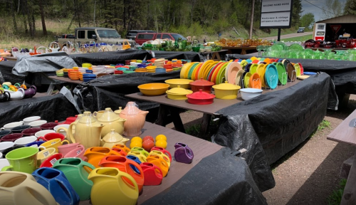 Colorful ceramic dishes and teapots displayed on tables covered with black tarps at an outdoor market.
