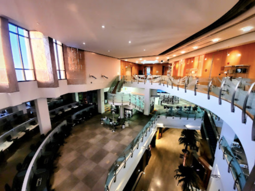 A spacious, modern interior of a building with multiple levels, glass railings, and large windows letting in natural light.