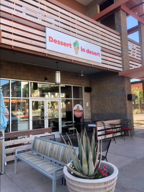 Exterior of a dessert shop named "Dessert in Desert," featuring a sign, seating area, and a potted plant.