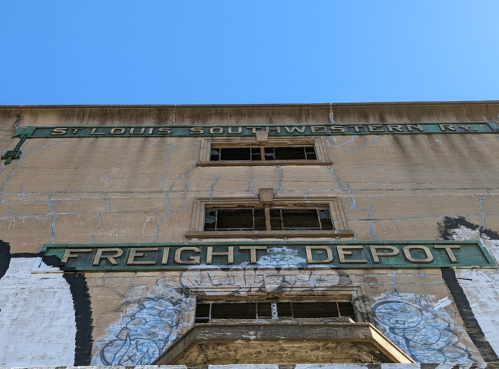 Abandoned freight depot building with faded signage against a clear blue sky.