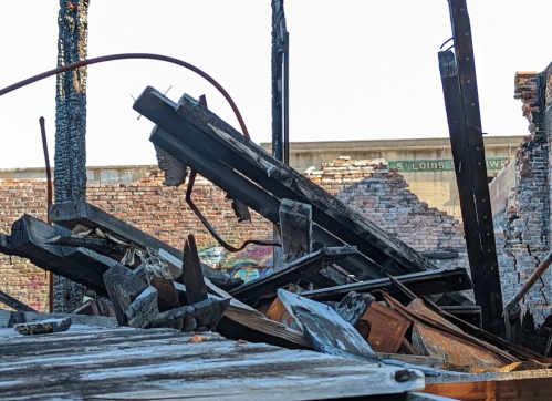 Debris from a collapsed structure, with charred wood and brick walls visible in the background.