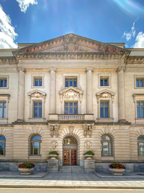 Historic building facade with grand columns, intricate sculptures, and a clear blue sky above.