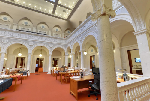 A spacious library interior with arched ceilings, marble columns, wooden tables, and warm lighting.