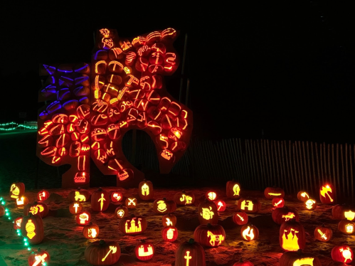 A large illuminated pumpkin sculpture of a knight on horseback surrounded by smaller carved pumpkins at night.