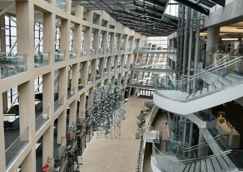 A modern library interior featuring curved architecture, large windows, and a hanging sculpture in the center.