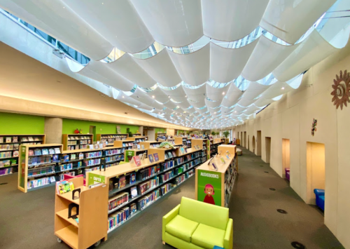 A modern library interior with colorful bookshelves, a green chair, and a wavy ceiling design.